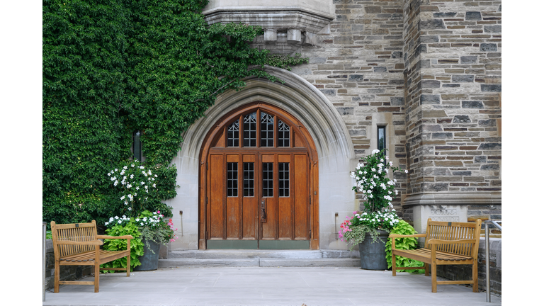 double wooden front door with leaded glass and ivy covered stone wall of gothic style college building