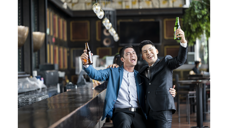 Two Businessman having fun while drinking a beer having a laugh at bar counter. Relax after hardworking day.