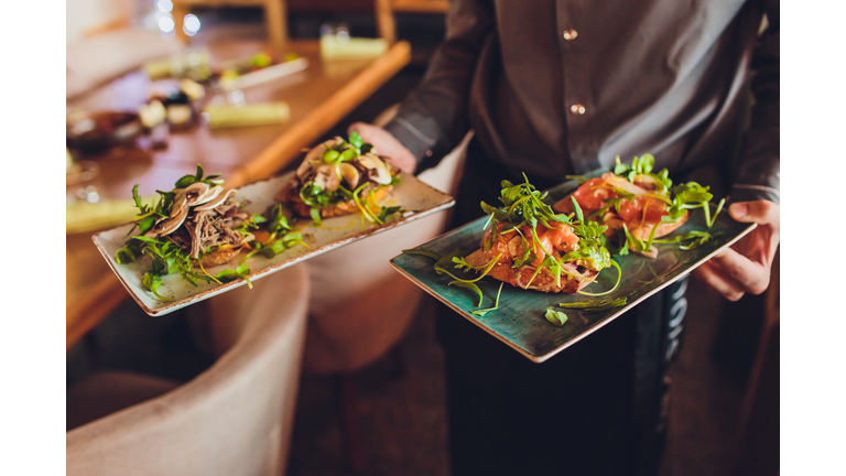 Two meat plate with salad leaves and summer salad in waiter's hand.