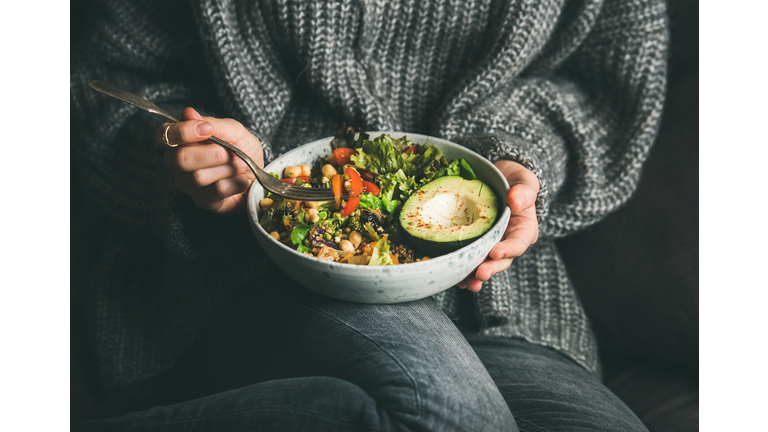 Woman in sweater eating fresh salad, avocado, beans and vegetables