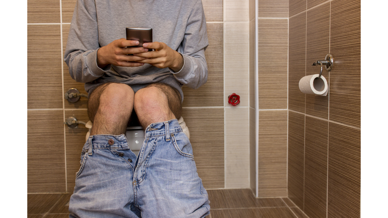 Low section of unrecognizable young man using phone in toilet