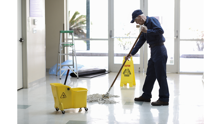 Senior Adult Janitor mops floor at entry to offices.