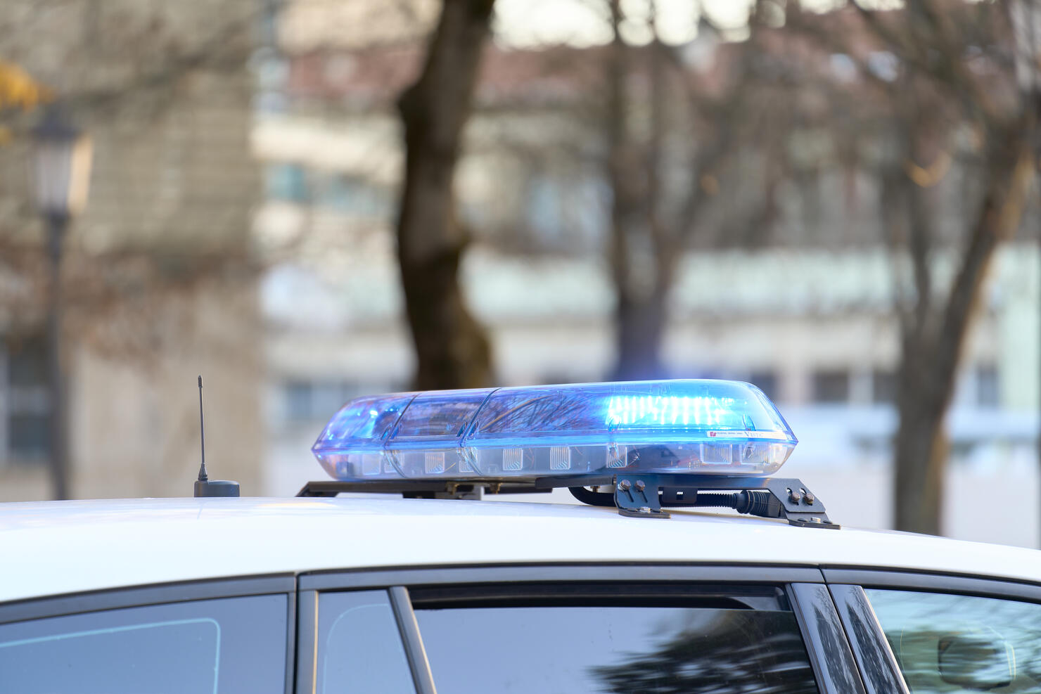 a close-up view of a police vehicle with blue lights patrolling near a public park with the windows and doors closed