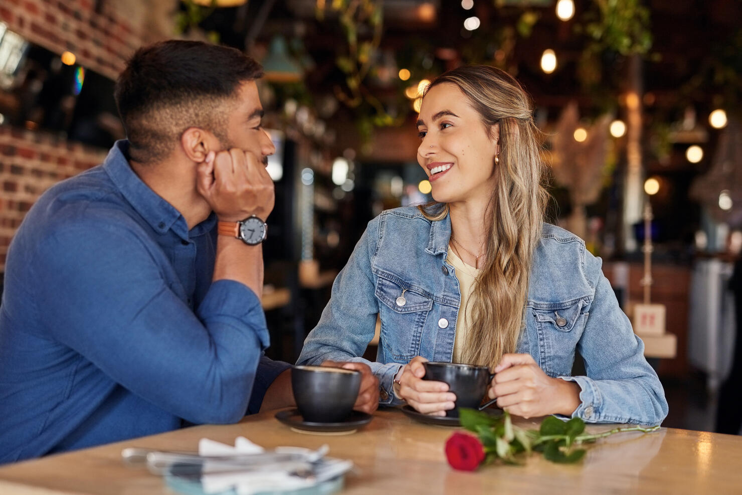 Coffee shop, date and couple of friends with rose for valentines day, anniversary or love in restaurant bokeh. Happy diversity people or woman with love partner at cafe at night for social talking