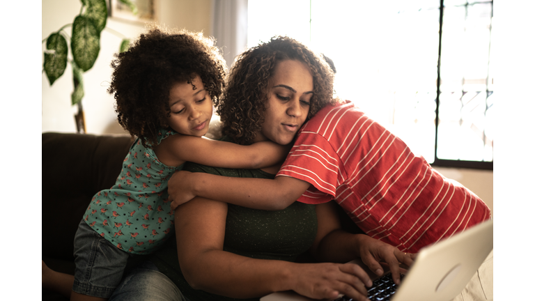 Mother trying to work with kids hugging her at home