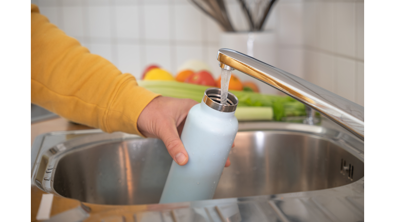 Man fills up reusable water bottle in the kitchen