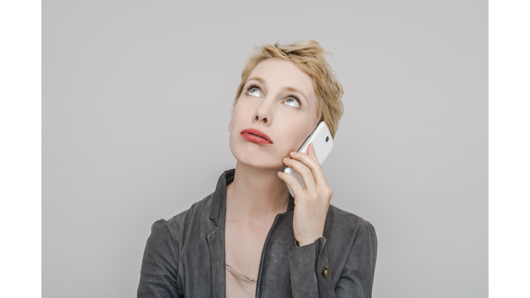 Portrait of blond woman with smartphone pouting mouth looking up