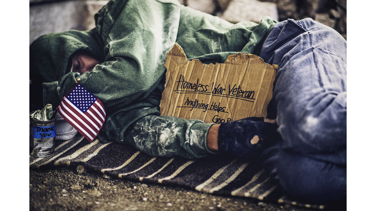 Fighting adversity. Homeless war veteran sleeping with sign and money tin