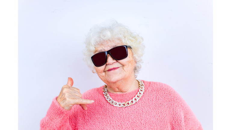 Portrait of funny senior blonde woman in sun glasses and pink sweater on white background