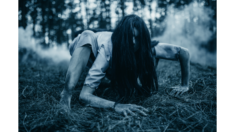 Girl in image of scary zombie crawls on ground in dark forest.