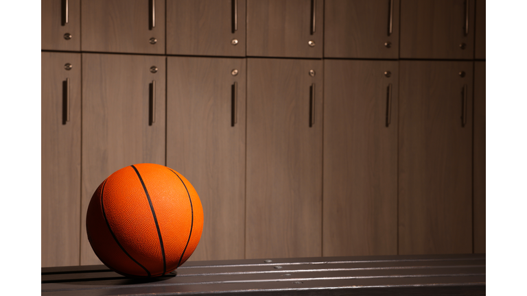 Orange basketball ball on wooden bench in locker room. Space for text