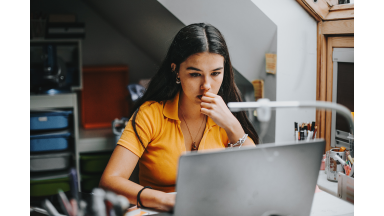 hispanic college student doing some home works from home with laptop