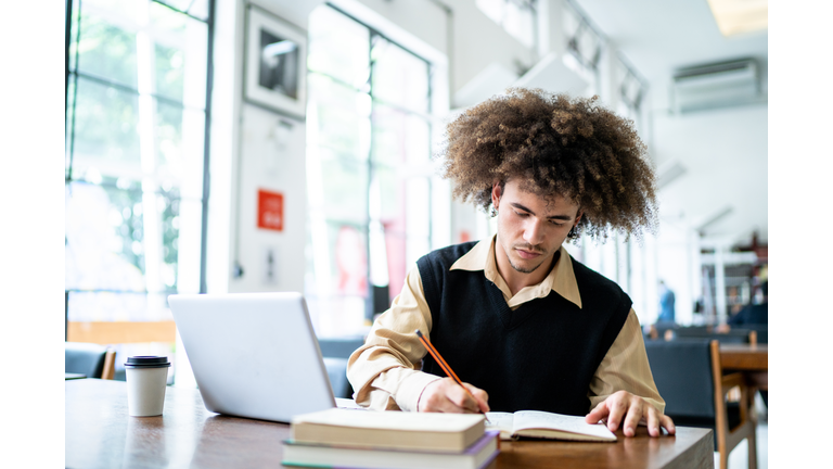 Young man studying using a laptop in a library