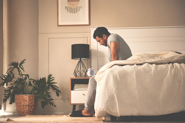 Depressed, stressed man waking up early in morning, sitting in bed and thinking, feeling anxious, nervous and unprepared. Suffering from mental disorder and feeling lost, confused, lonely, detached