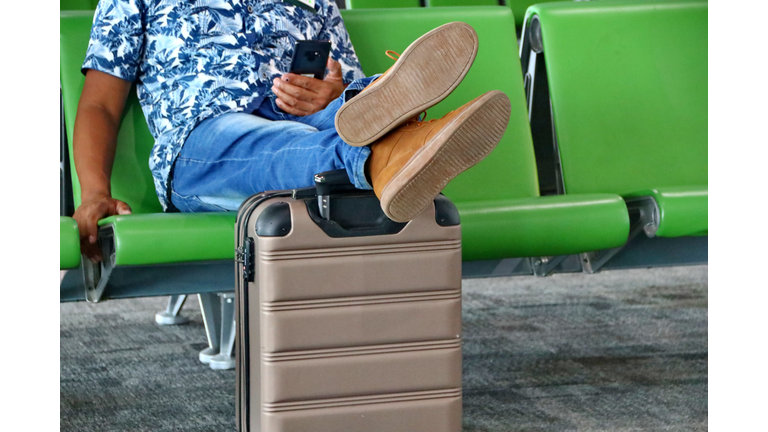 A Passenger Sitting In A Chair, Resting While Resting His Feet On His Suitcase