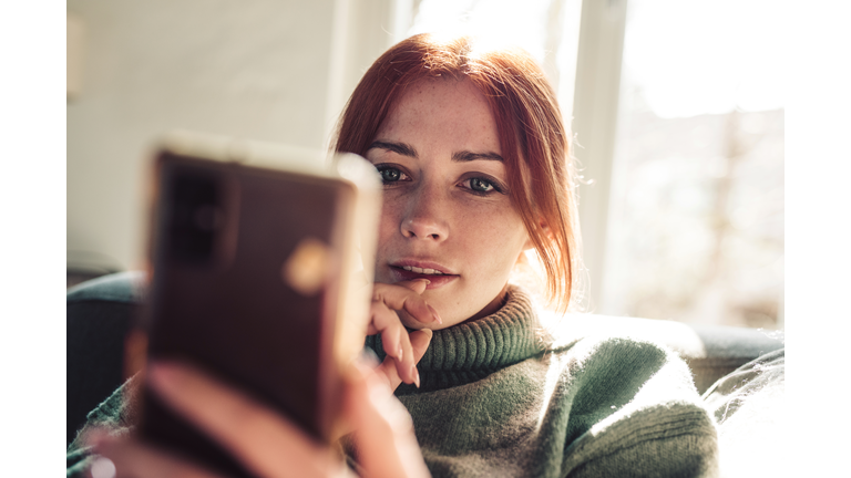 Woman with red hair looking on screen of her mobile phone.