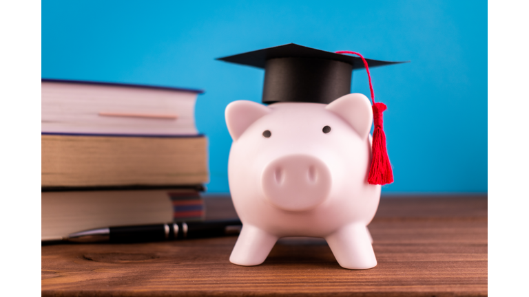 Piggy bank with a graduation hat and a lot of books and a pen on a light blue backround. Student scolarship save concept. Finance concept.