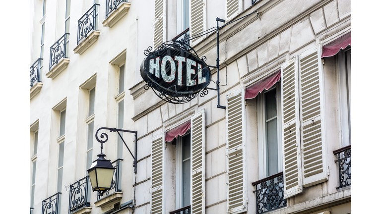 The vintage sign of a modest hotel in an old building with a period street light in Paris.