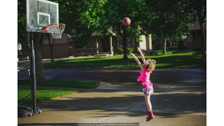 Girl throwing baseball at basketball hoop