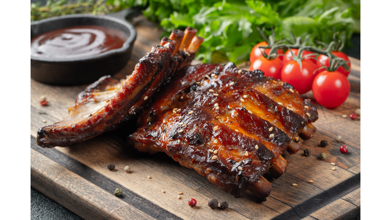 Closeup of pork ribs grilled with BBQ sauce and caramelized in honey. Tasty snack to beer on a wooden Board for filing on dark concrete background