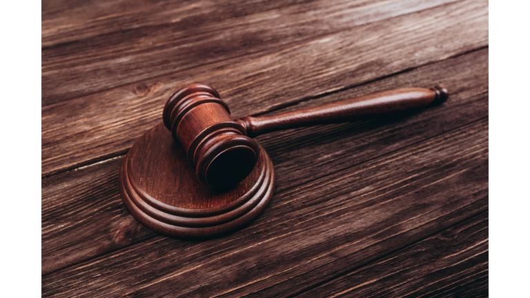 Brown judge's gavel over stand against wooden background.