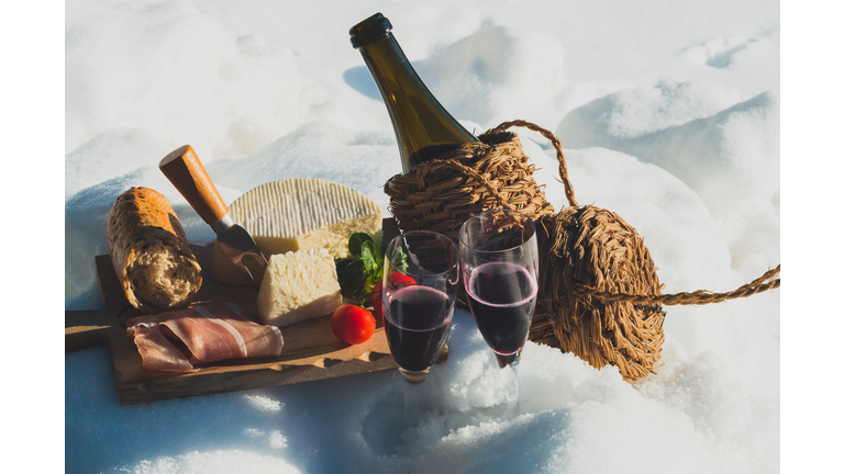 Romantic picnic with Lambrusco cheese baguette and ham on snow. Traditional Italian food and drink in sunny winter day.