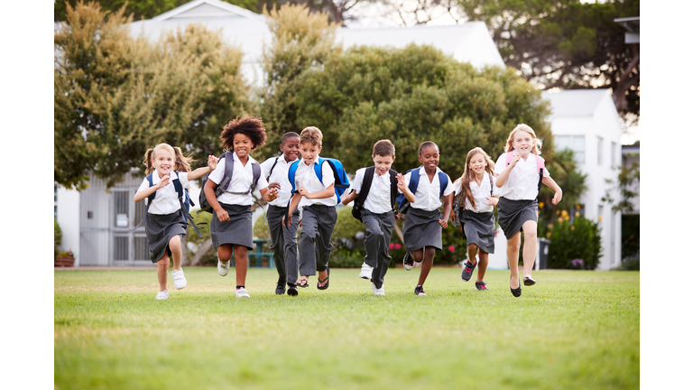 Excited Elementary School Pupils Wearing Uniform Running Across Field At Break Time
