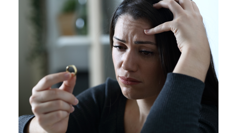 Sad doubtful wife looks at wedding ring thinking in divorce