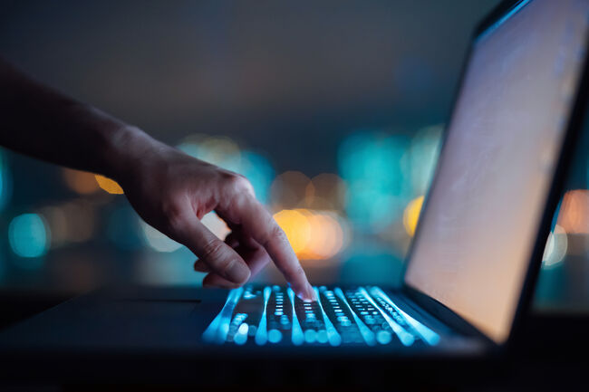 Close up of woman's hand typing on computer keyboard in the dark against colourful bokeh in background, working late on laptop at home