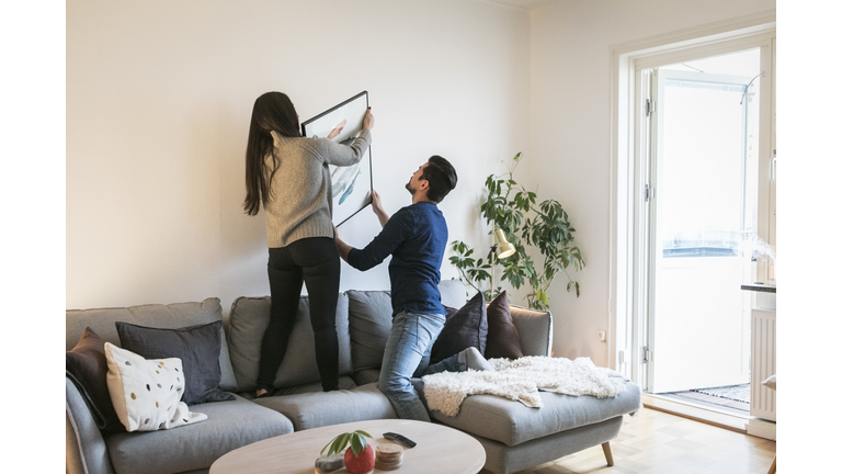 Couple adjusting painting on wall while leaning on sofa at home