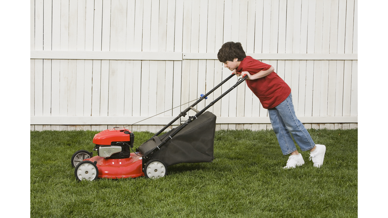 Mixed Race boy pushing lawn mower