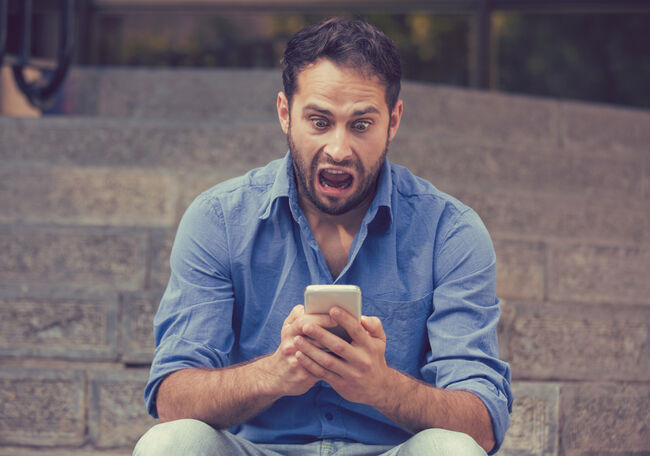 Upset man looking at his mobile phone sitting on steps outdoors