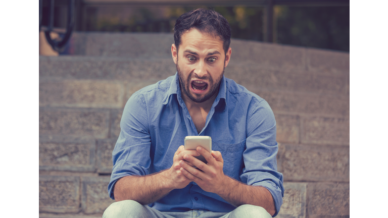 Upset man looking at his mobile phone sitting on steps outdoors