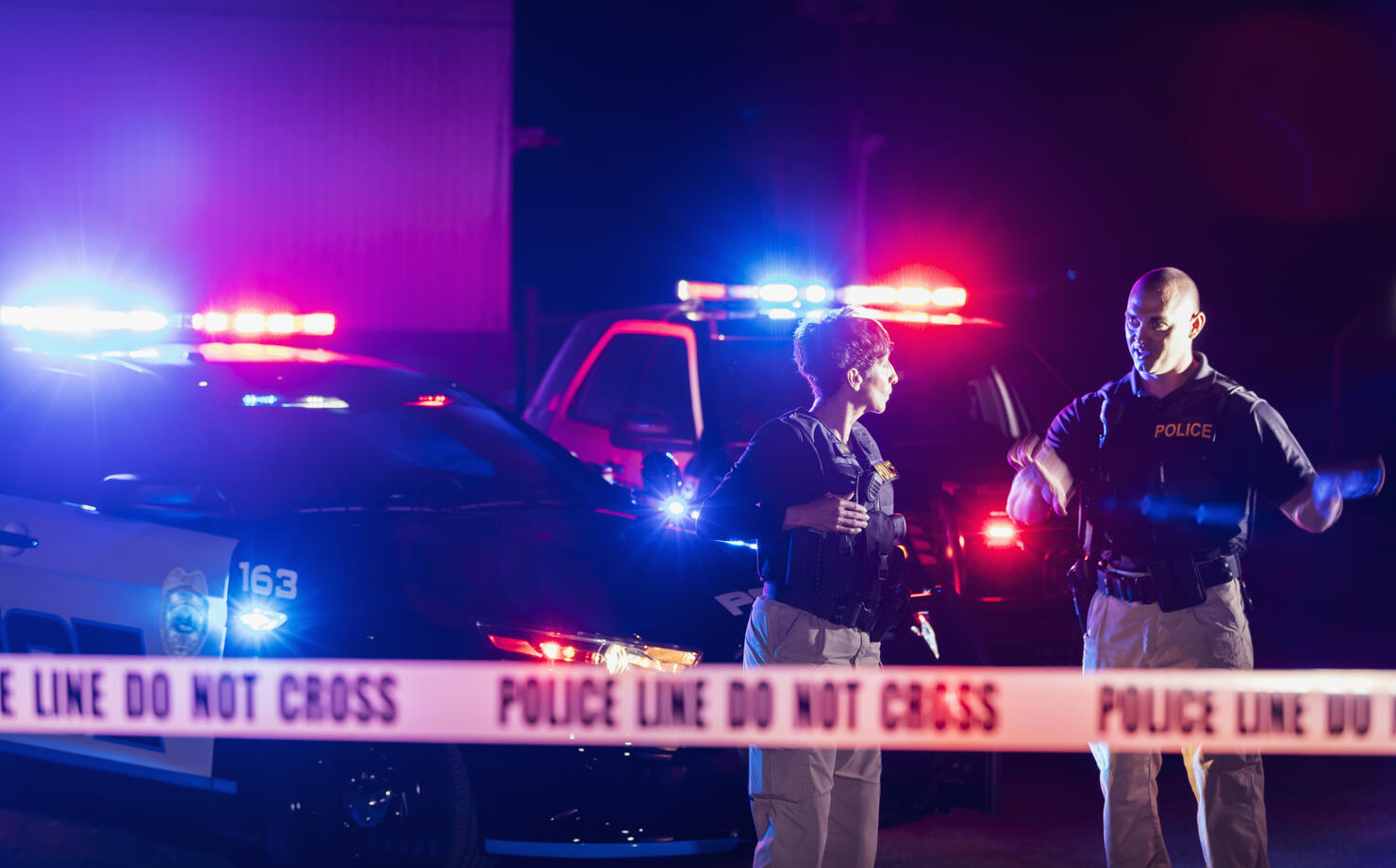 Two police officers standing in front of patrol cars