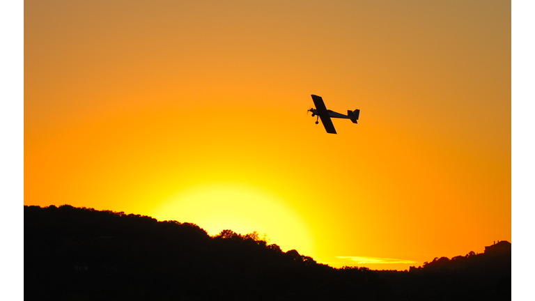 Under side of an airplane flying in an orange sky at sunset