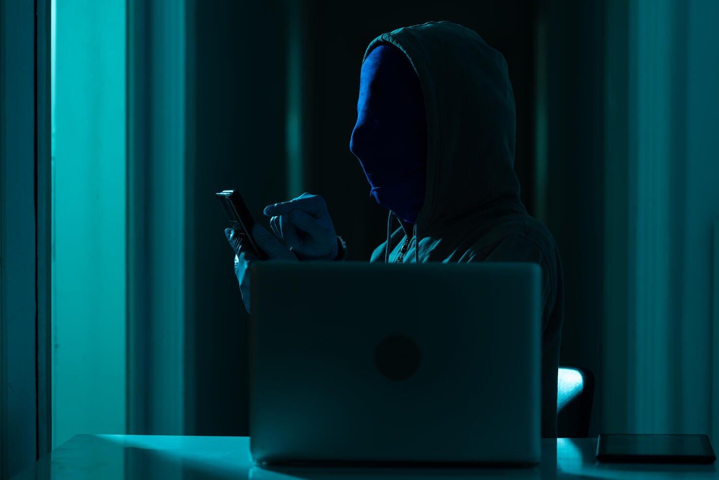 Man Wearing Hooded Shirt And Mask Using Laptop In Dark To Hack
