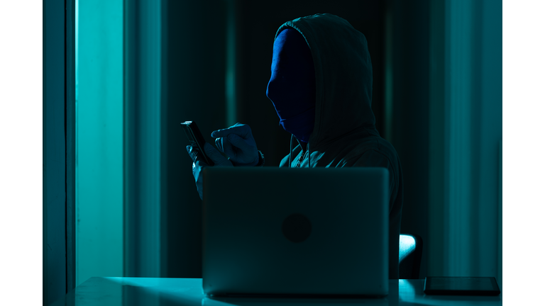 Man Wearing Hooded Shirt And Mask Using Laptop In Dark To Hack