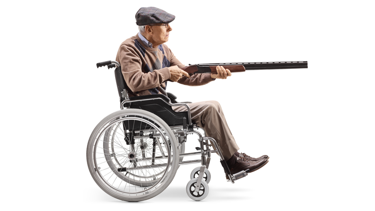 Elderly man in a wheelchair aiming with a shotgun