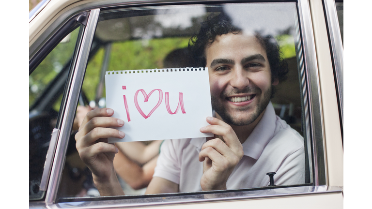 Man in car holding sign saying 'I love you'