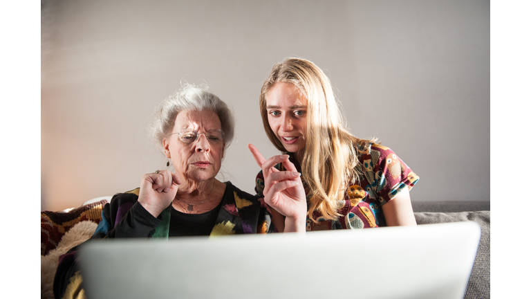 Young woman showing senior lady how to work laptop