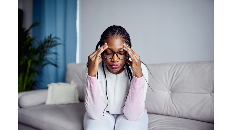 A young girl is sitting on the couch at home with her head in her hands.