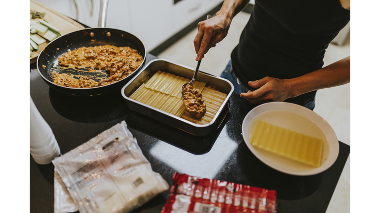 Woman making lasagna while standing in kitchen at home