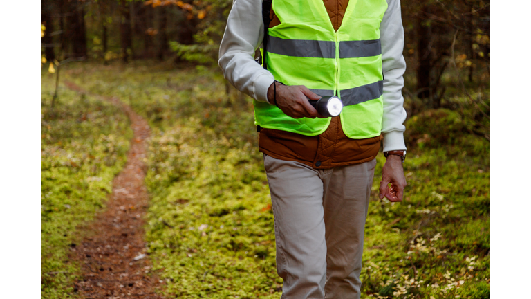 Male Volunteer of the Search and Rescue Team Dressed in a Signal Vest with a Flashlight in the Forest.