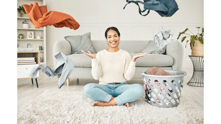 Portrait of a cleaning, carefree female cleaner throwing clothing in the air. Happy, smiling and young woman doing laundry, washing clothes and sitting in a messy living room at home.