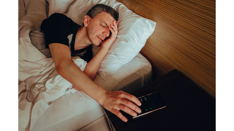 Adult man asleep turning off his cell phone alarm