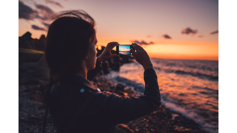 Woman at the beach photographing the sunset