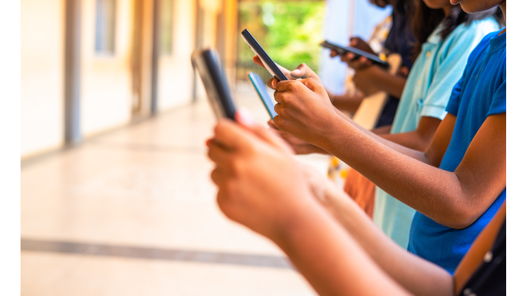 Close up shot, group of children hands busy using smartphone at school corridor - concept of social media, playing games, technology and education