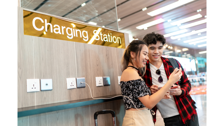 Young Asian couple enjoying free phone charge sharing at the airport