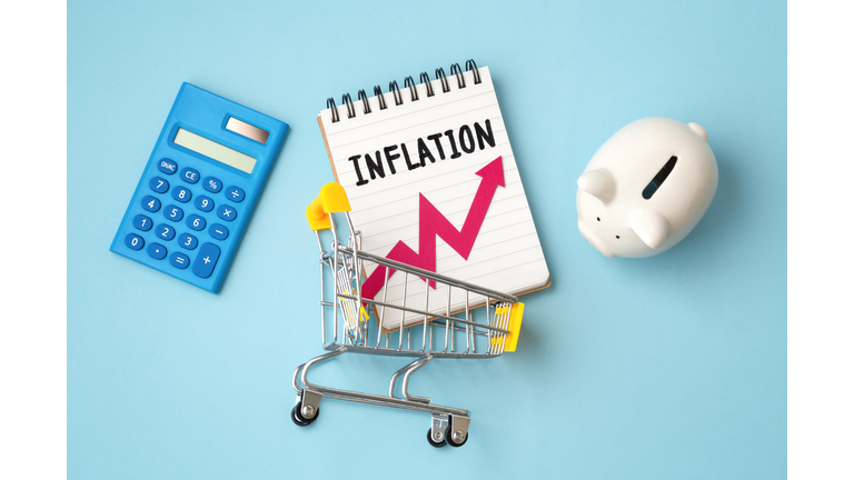 Inflation word on notebook and red graph going up in shopping cart  with calculator and piggy bank on blue background