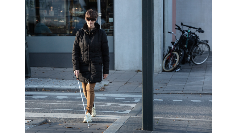 Full length of blind woman crossing road with stick in city